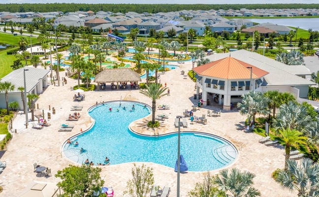 Complexe de piscines d’un resort avec palmiers, toboggan, club-house et maisons résidentielles autour d’un quartier en bord de lac